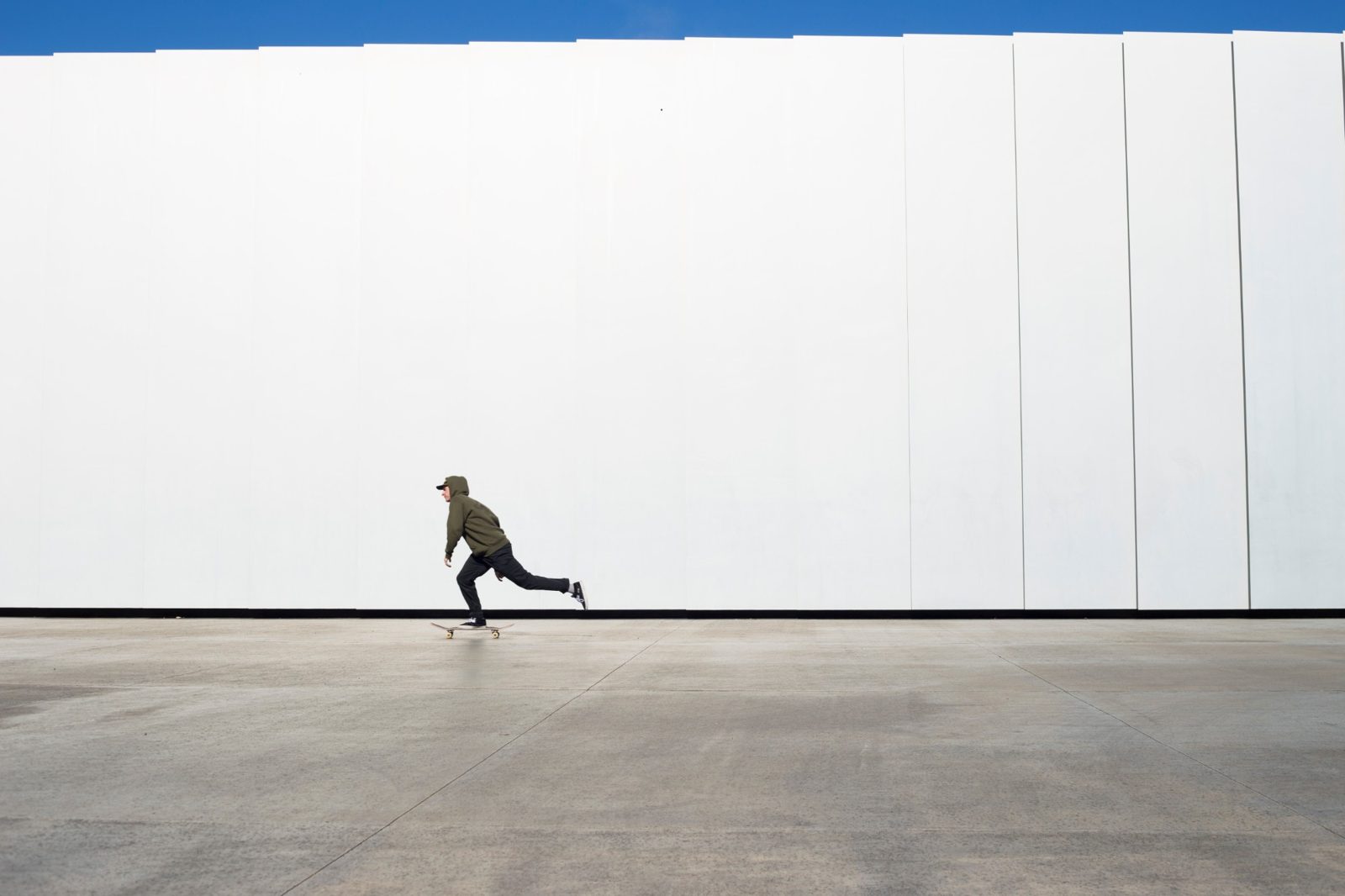 Austin skateboarding past a tall white wall